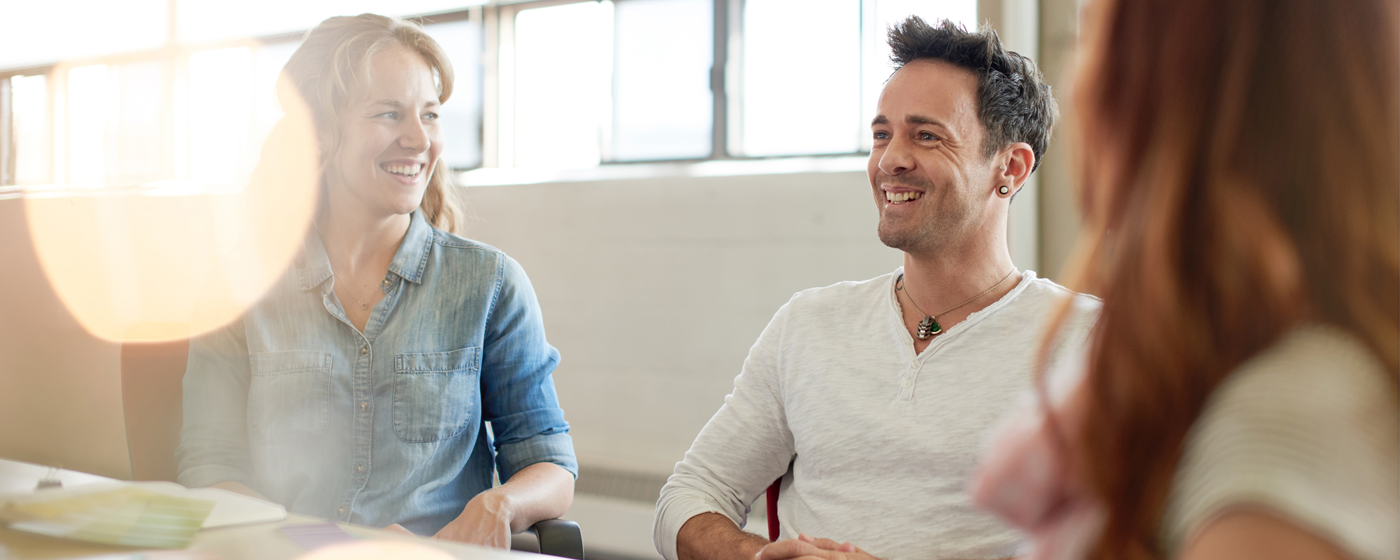 Three people sitting at a conference table with sunlight flowing into the room.