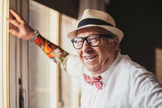 Older, tattooed man posing against a door frame